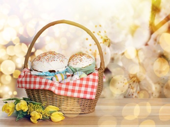 Basket with delicious Easter cakes, painted eggs and flowers on wooden table. Space for text