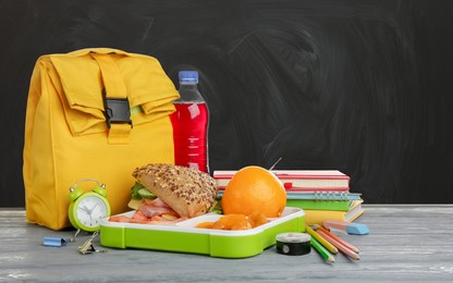 Composition with lunch box and food on wooden table near blackboard