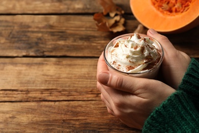 Woman holding tasty pumpkin latte at wooden table, closeup. Space for text
