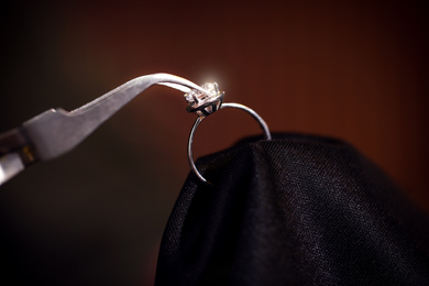 Working with beautiful ring on dark background, closeup. Jeweler's workshop