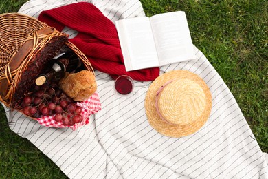 Flat lay composition with wicker basket and picnic blanket on green grass
