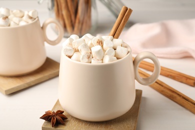 Cup of hot drink with marshmallows and aromatic cinnamon on white table