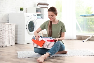 Young woman with basket of clean laundry on floor in room