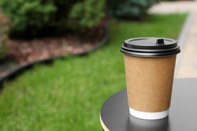 Photo of Cardboard cup with plastic lid on black table in park, space for text. Coffee to go