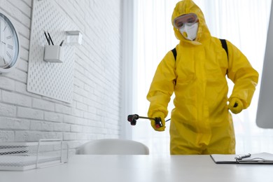 Employee in protective suit sanitizing office. Medical disinfection, focus on spray