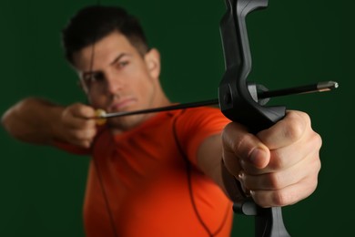 Man with bow and arrow practicing archery against green background, focus on hand