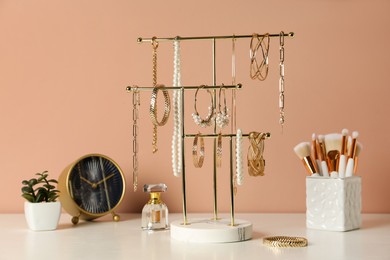 Holder with set of luxurious jewelry on dressing table near pale pink wall