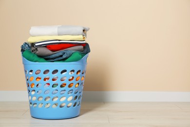 Photo of Plastic laundry basket with clean clothes on floor near beige wall. Space for text