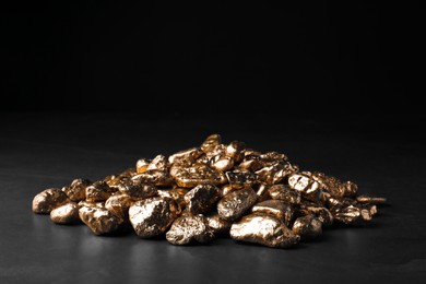 Pile of gold nuggets on black table against dark background, space for text