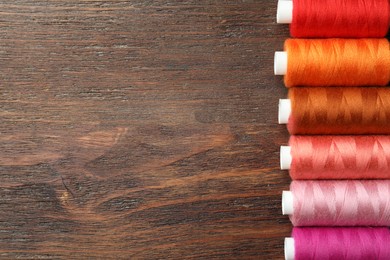Set of colorful sewing threads on wooden table, flat lay. Space for text