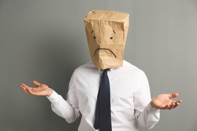 Man wearing paper bag with drawn sad face on grey background
