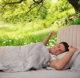 Happy man stretching in bed and beautiful view of park on background. Sleep well - stay healthy