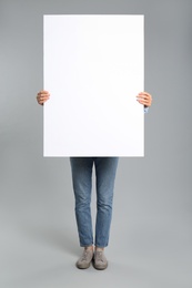 Woman holding white blank poster on grey background. Mockup for design
