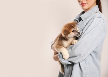 Woman holding Akita Inu puppy on light background, closeup. Space for text