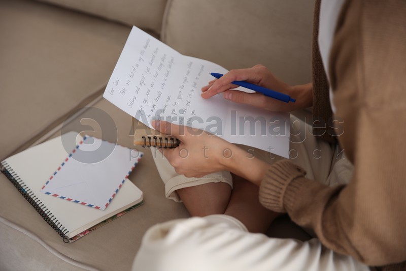 Woman writing letter while sitting on sofa at home, closeup