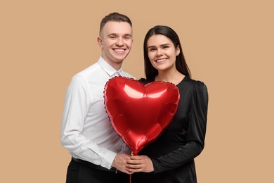 Photo of Lovely couple with heart shaped balloon on beige background. Valentine's day celebration