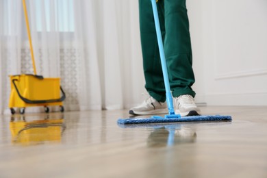 Professional janitor cleaning parquet floor with mop indoors, closeup. Space for text