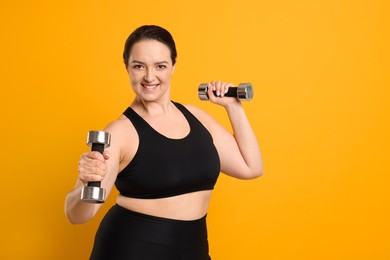 Photo of Happy overweight woman doing exercise with dumbbells on orange background