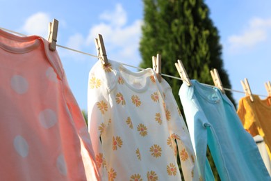 Clean baby onesies hanging on washing line outdoors. Drying clothes