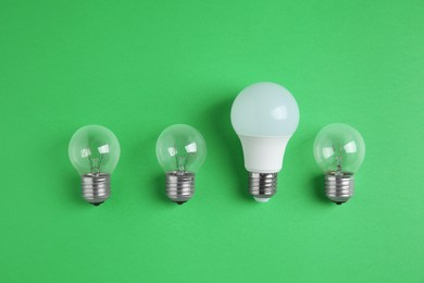 LED light bulb and simple ones on green background, flat lay. Energy saving concept