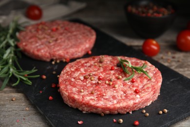 Raw hamburger patties with rosemary and peppercorns on wooden table, closeup