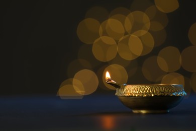 Photo of Lit diya lamp on dark table, space for text. Diwali celebration