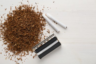 Photo of Roller, tobacco and hand rolled cigarettes on white wooden table, flat lay with space for text
