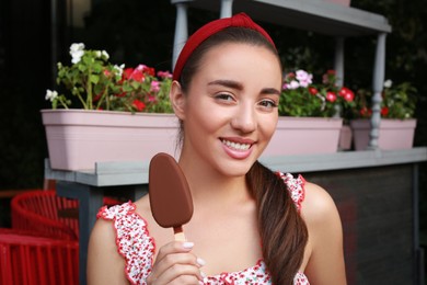 Beautiful young woman holding ice cream glazed in chocolate on city street