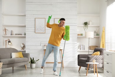 Man in headphones with mop singing while cleaning at home