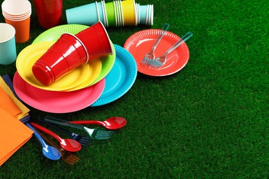 Disposable tableware on green artificial grass. Space for text
