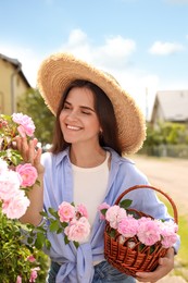 Photo of Happy young woman with basket of pink tea roses in blooming garden
