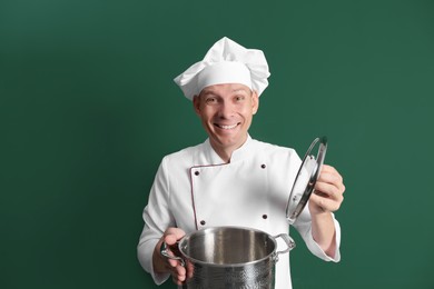 Happy male chef with cooking pot on dark green background