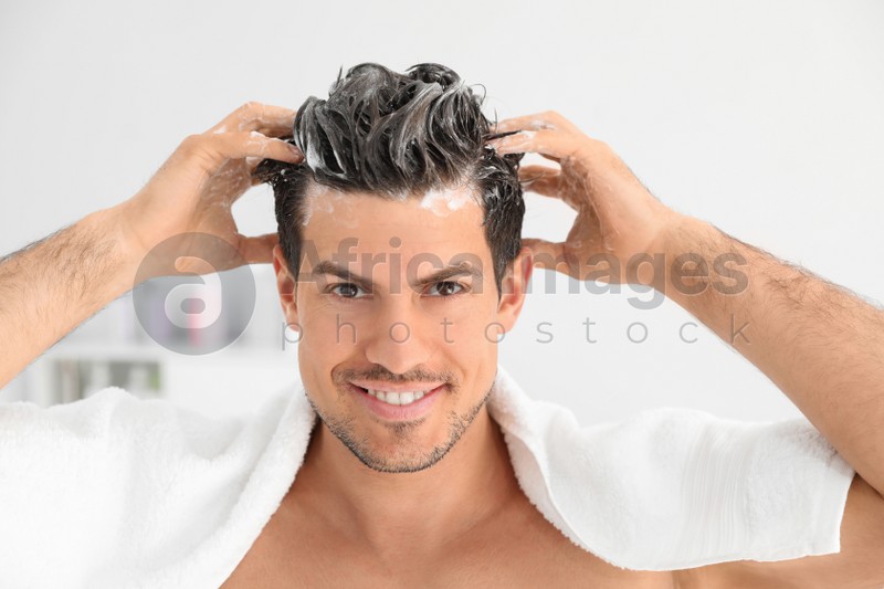 Man applying shampoo onto his hair against light background