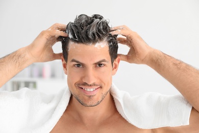 Man applying shampoo onto his hair against light background