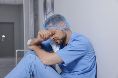 Photo of Exhausted doctor near grey wall in hospital corridor