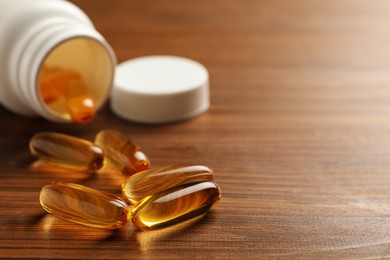 Dietary supplement capsules on wooden table, closeup. Space for text