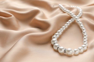 Elegant necklace with pearls on beige silk, closeup. Space for text