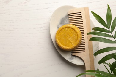 Solid shampoo bar, hair comb and green branch on white wooden table, top view. Space for text