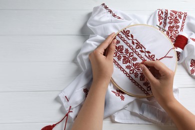 Woman embroidering shirt with red thread at white wooden table, top view and space for text. Ukrainian national clothes