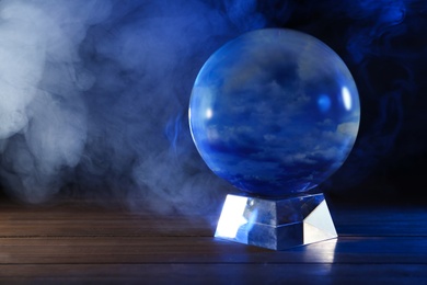 Magic crystal ball on wooden table and smoke against dark background, space for text. Making predictions