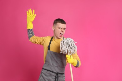 Handsome young man with mop singing on pink background