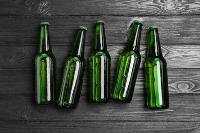 Photo of Glass bottles of beer on black wooden background, flat lay