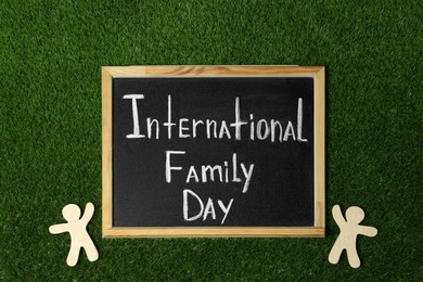 Chalkboard with text International Family Day and wooden figures on green grass, flat lay