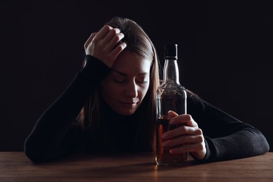 Alcohol addiction. Woman with bottle of whiskey at wooden table