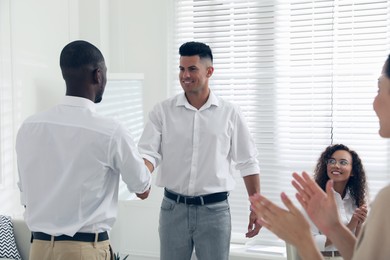 Boss shaking hand with new employee and coworkers applauding in office