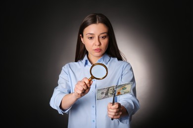 Photo of Expert authenticating 100 dollar banknote with magnifying glass against dark background. Fake money concept