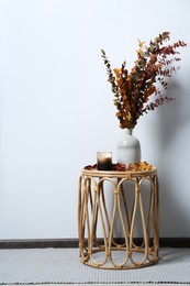Vase with branches and candle on table near white wall, space for text