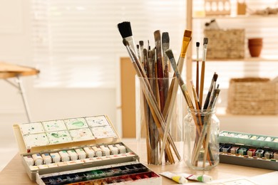 Different brushes and colorful paints on wooden table in studio. Artist's workplace