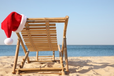 Photo of Sun lounger with Santa's hat on beach, space for text. Christmas vacation