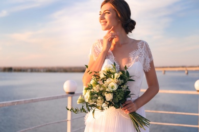 Gorgeous bride in beautiful wedding dress with bouquet near river, focus on flowers